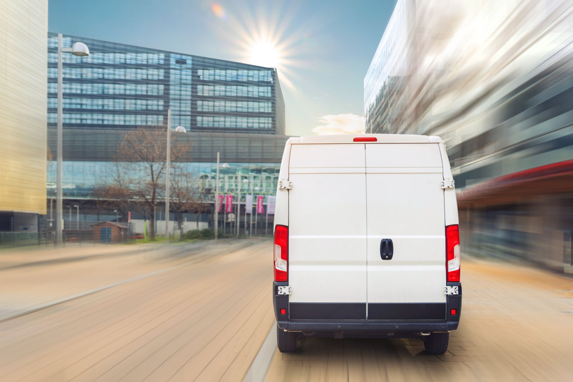 Courier wearing mask unloads packages from white delivery van during the day.